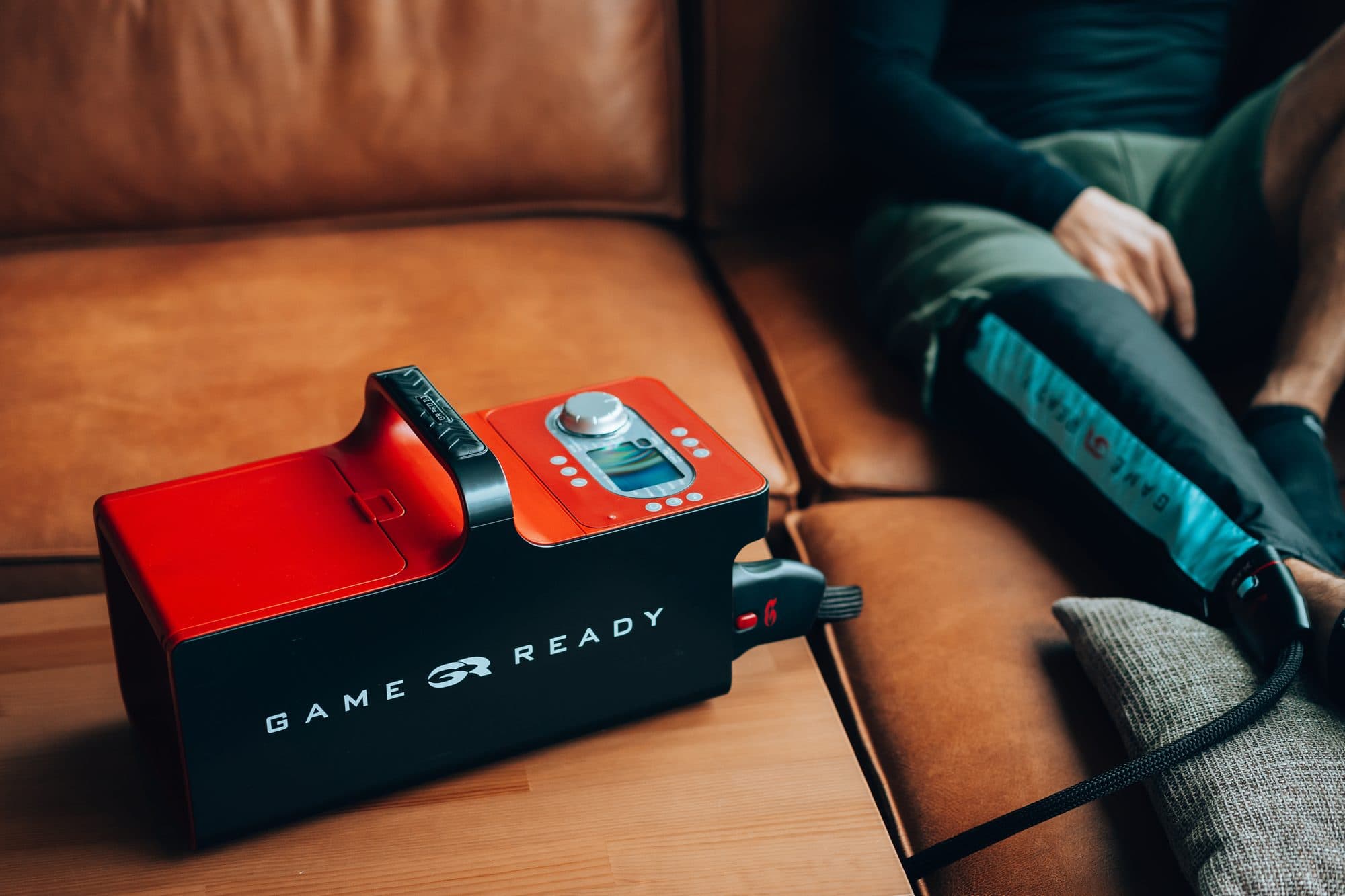 Game Ready GRPro 2.1 Steuergerät auf einem Holztisch, im Hintergrund eine angelegte Manschette